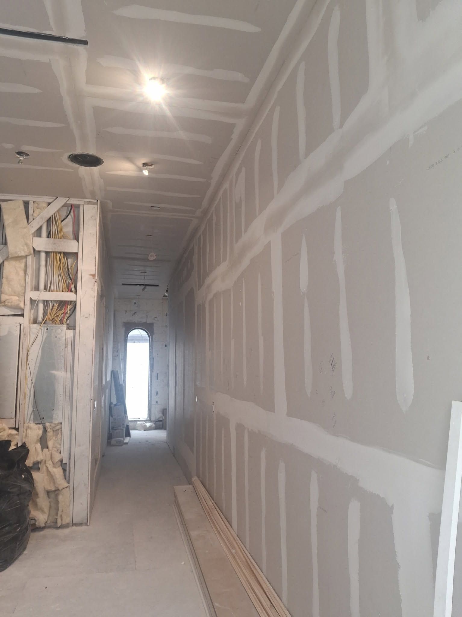 A long hallway with sheetrock hung, the seams taped and mudded, before paint.
